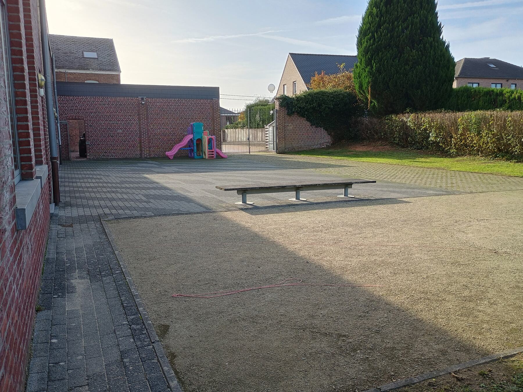 Petanquebaan, zitbank en speeltuig achter het gebouw